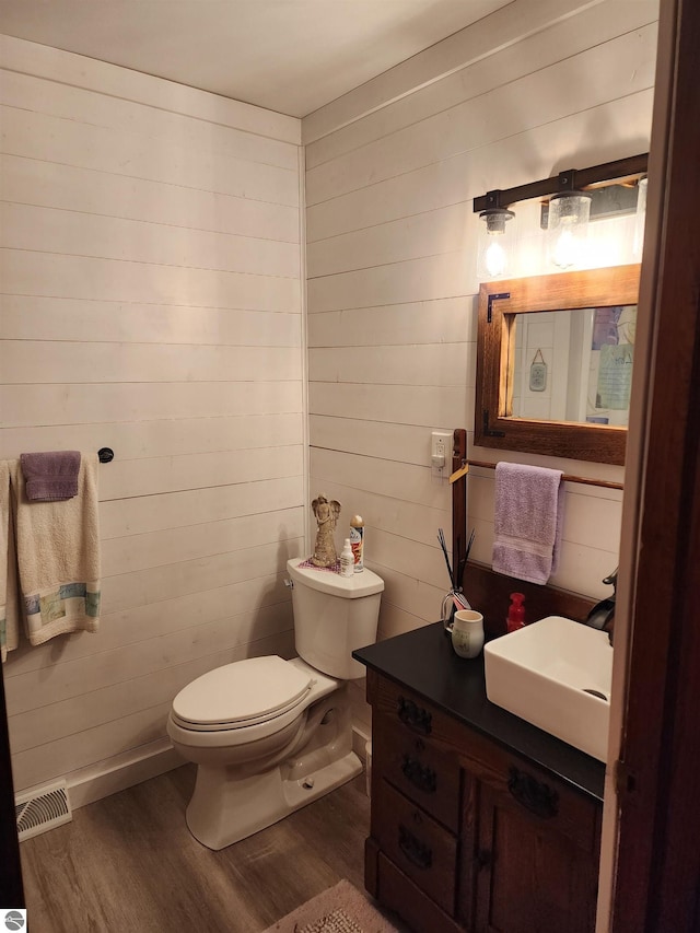 bathroom featuring hardwood / wood-style flooring, wooden walls, vanity, and toilet