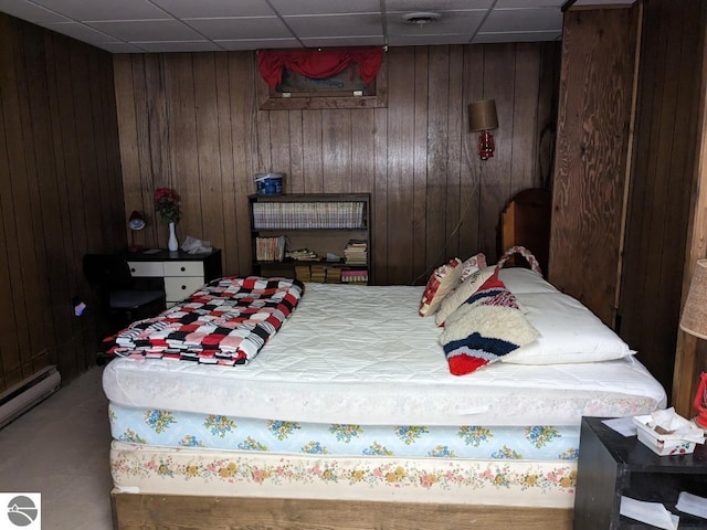 bedroom featuring a drop ceiling, wood walls, and baseboard heating