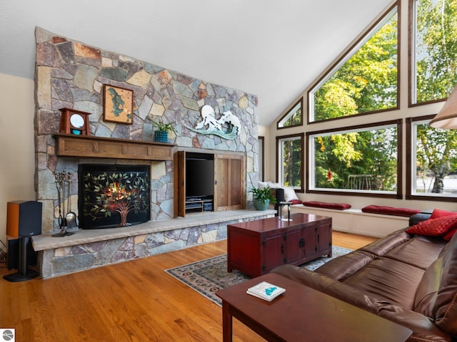 living room with hardwood / wood-style flooring, high vaulted ceiling, and a stone fireplace