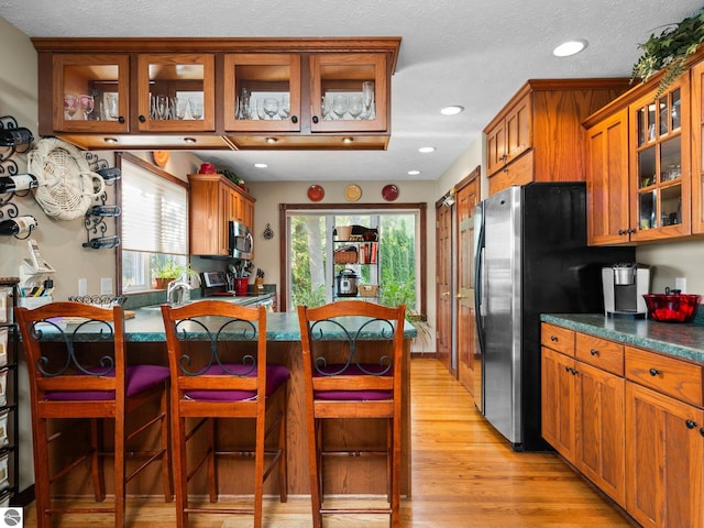 kitchen with a breakfast bar area, light hardwood / wood-style flooring, stainless steel appliances, and a textured ceiling