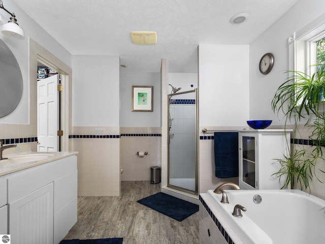 bathroom featuring separate shower and tub, tile walls, hardwood / wood-style flooring, vanity, and a textured ceiling