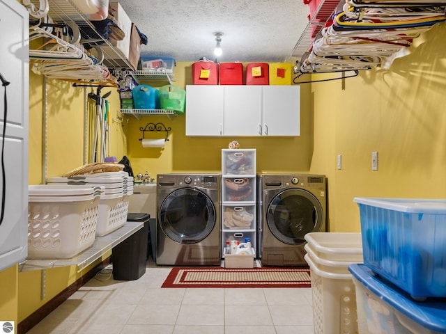 clothes washing area featuring washing machine and clothes dryer, cabinets, light tile patterned floors, and a textured ceiling