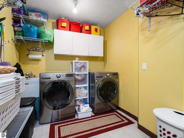 laundry area featuring light tile patterned flooring, washing machine and dryer, cabinets, and a textured ceiling