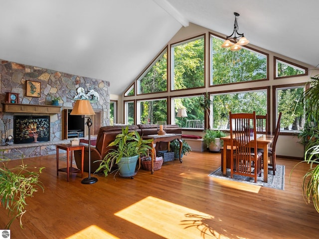 living room with high vaulted ceiling, hardwood / wood-style flooring, beamed ceiling, and a stone fireplace