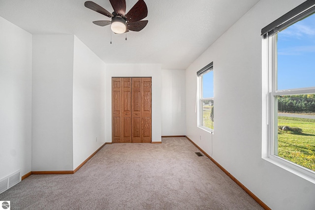 unfurnished bedroom featuring a closet, light colored carpet, a textured ceiling, and ceiling fan