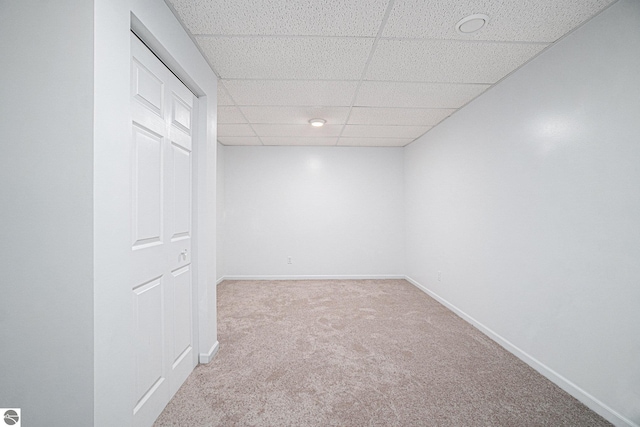 basement featuring a paneled ceiling and light colored carpet