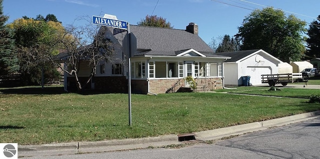 view of front facade featuring a front yard, a garage, a porch, and an outbuilding