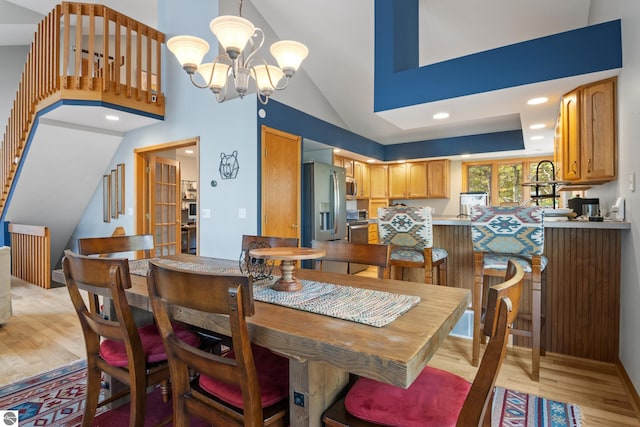 dining area with a notable chandelier, light hardwood / wood-style flooring, and high vaulted ceiling