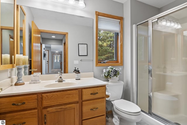 bathroom featuring a shower with shower door, vanity, and toilet