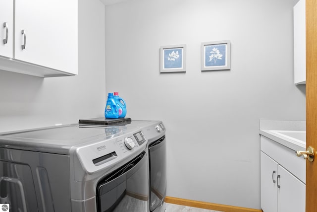 washroom featuring sink, independent washer and dryer, light hardwood / wood-style flooring, and cabinets