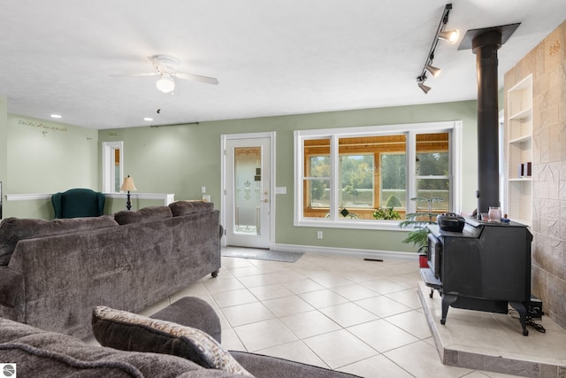 living room with a wood stove, track lighting, light tile patterned floors, and ceiling fan