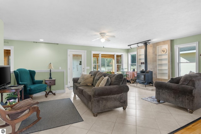 tiled living room featuring rail lighting, ceiling fan, and a wood stove