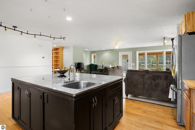 kitchen with stainless steel refrigerator, a kitchen island with sink, sink, light hardwood / wood-style floors, and ceiling fan