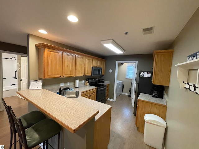 kitchen with light hardwood / wood-style floors, washer and dryer, black / electric stove, sink, and kitchen peninsula