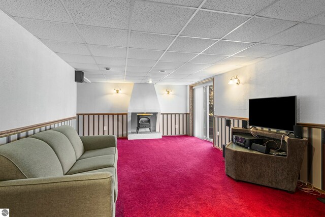 living room featuring carpet floors, a drop ceiling, and a wood stove