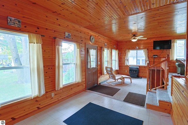 entryway featuring ceiling fan, wood ceiling, wooden walls, and a wood stove