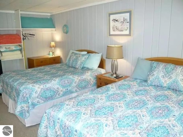 bedroom with ornamental molding, wood walls, and carpet flooring