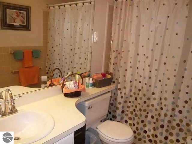 bathroom featuring curtained shower, tile walls, vanity, and toilet