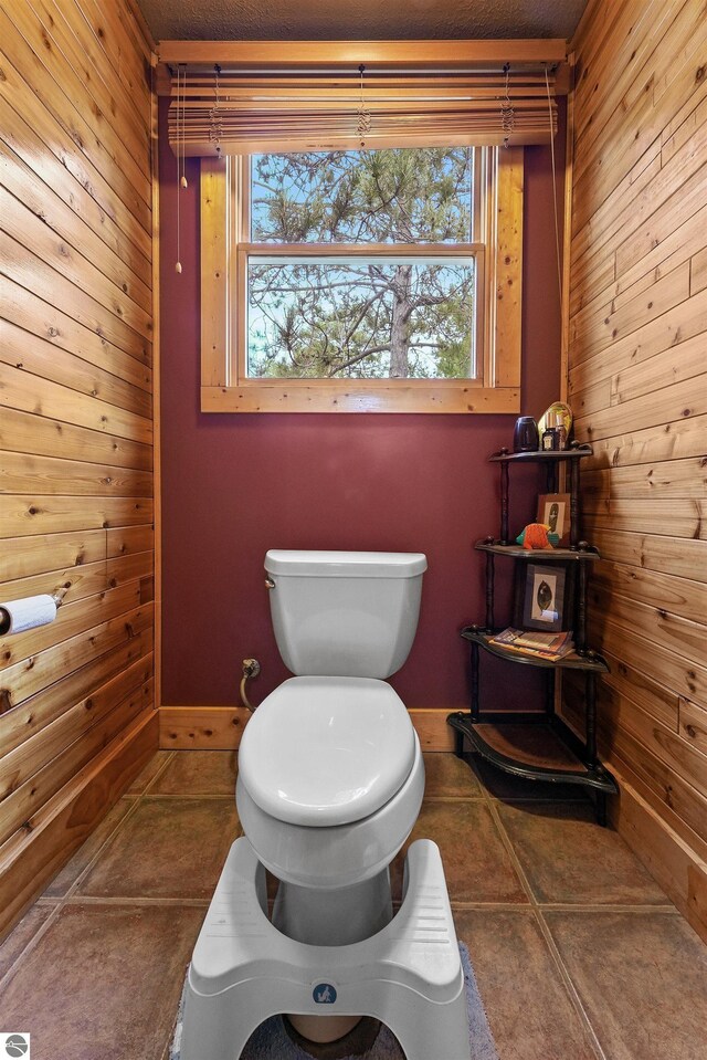 bathroom with wood walls, toilet, and tile patterned floors