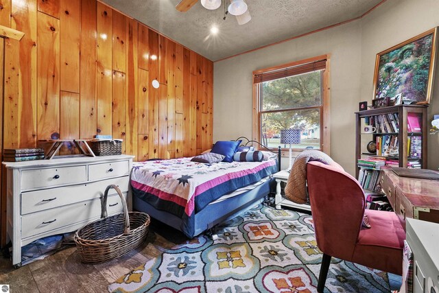 bedroom featuring ceiling fan, a textured ceiling, and wooden walls