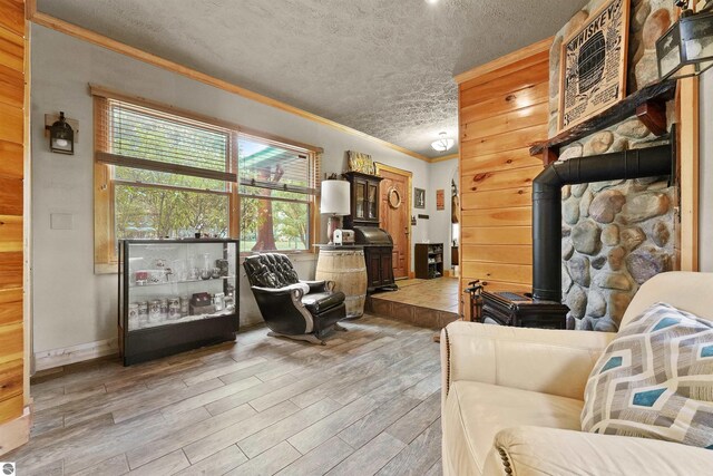 living room with wooden walls, a wood stove, light hardwood / wood-style floors, ornamental molding, and a textured ceiling