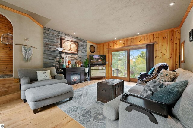 living room with a fireplace, light wood-type flooring, crown molding, and wood walls