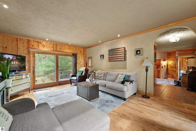 living room featuring light hardwood / wood-style floors, crown molding, wooden walls, and a textured ceiling