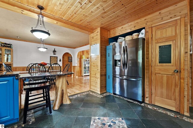 kitchen with hanging light fixtures, wood walls, ornamental molding, blue cabinets, and stainless steel refrigerator with ice dispenser