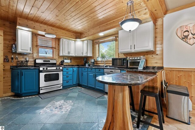 kitchen featuring white gas range oven, blue cabinetry, white cabinets, and wooden walls