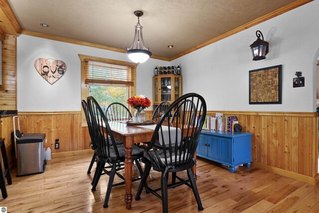 dining room with a textured ceiling, wooden walls, crown molding, and light hardwood / wood-style floors