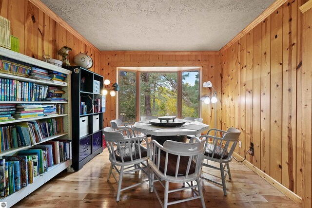 dining space with crown molding, wood walls, and light hardwood / wood-style flooring