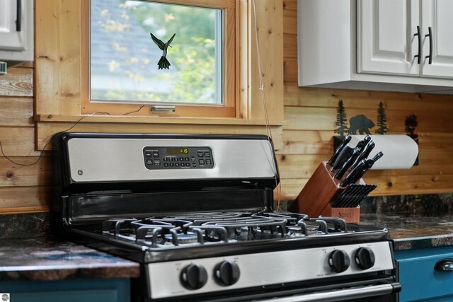 kitchen featuring wood walls, white cabinets, and stainless steel gas range oven