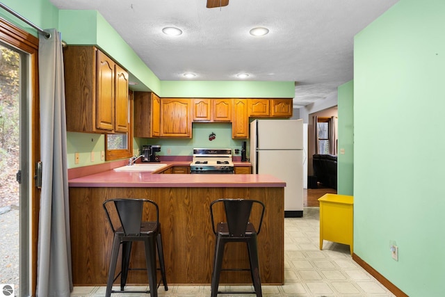 kitchen featuring kitchen peninsula, sink, a kitchen bar, stove, and white fridge