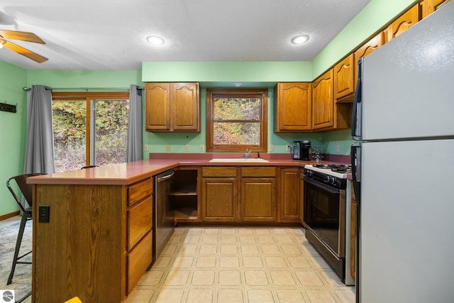 kitchen with plenty of natural light, kitchen peninsula, black gas range oven, and white refrigerator