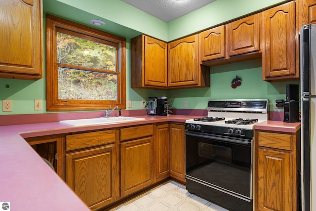 kitchen featuring white range with gas stovetop, sink, a textured ceiling, and black fridge