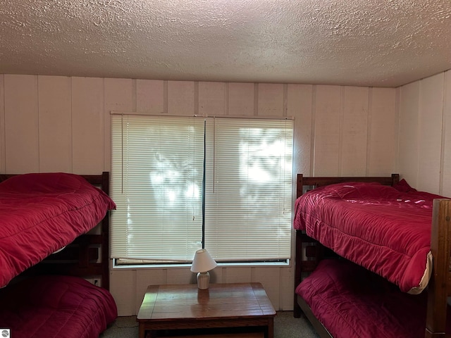 bedroom featuring carpet flooring, a textured ceiling, and wood walls