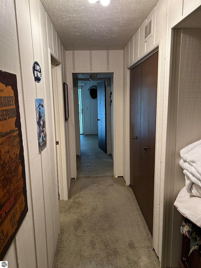 hallway with light colored carpet and a textured ceiling