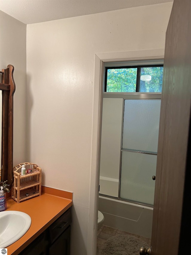 full bathroom featuring tile patterned flooring, combined bath / shower with glass door, a textured ceiling, toilet, and vanity