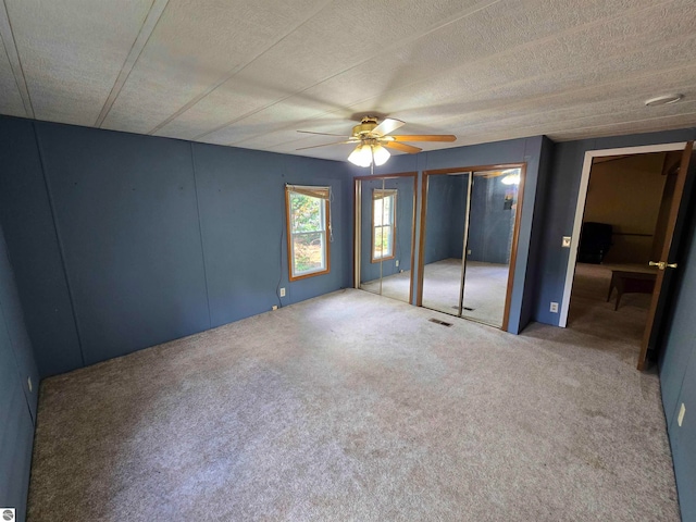 unfurnished bedroom featuring two closets, carpet flooring, and ceiling fan