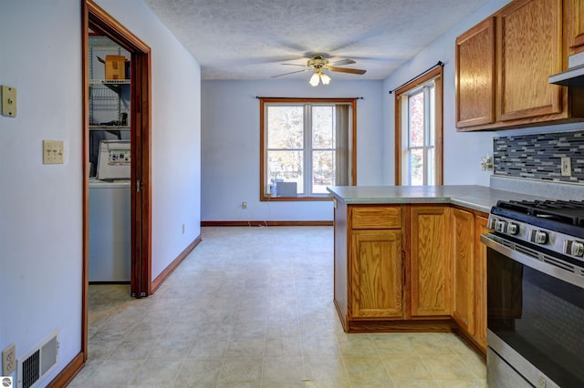 kitchen with backsplash, stainless steel range with gas cooktop, ceiling fan, washer / dryer, and kitchen peninsula