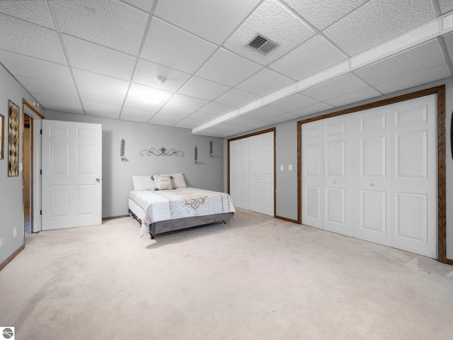 carpeted bedroom featuring a paneled ceiling and multiple closets