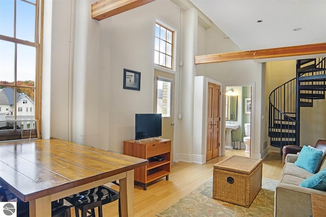 living room featuring beam ceiling, a towering ceiling, and light hardwood / wood-style floors