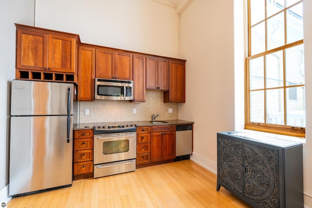 kitchen featuring brown cabinets, decorative backsplash, light wood-style flooring, a sink, and appliances with stainless steel finishes