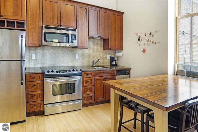 kitchen featuring appliances with stainless steel finishes, sink, dark stone counters, and light hardwood / wood-style floors