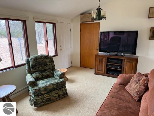 living area featuring light colored carpet, a baseboard radiator, vaulted ceiling, and a chandelier