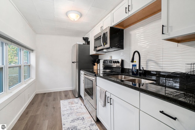 kitchen with white cabinets, wood finished floors, a sink, and appliances with stainless steel finishes