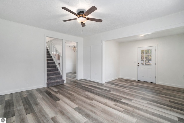 unfurnished living room featuring wood finished floors, baseboards, a textured ceiling, stairs, and ceiling fan with notable chandelier