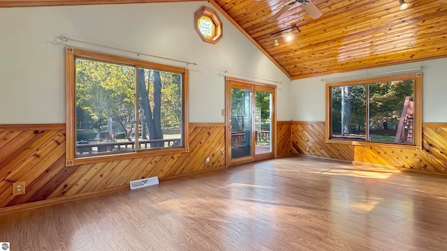 spare room featuring wood walls, plenty of natural light, hardwood / wood-style floors, and ceiling fan