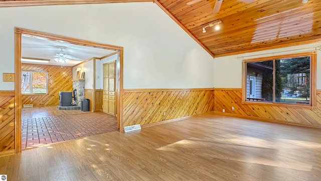 unfurnished room with a wood stove, wood-type flooring, wood ceiling, and ceiling fan