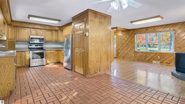 kitchen with wooden walls, decorative backsplash, stainless steel appliances, and ceiling fan